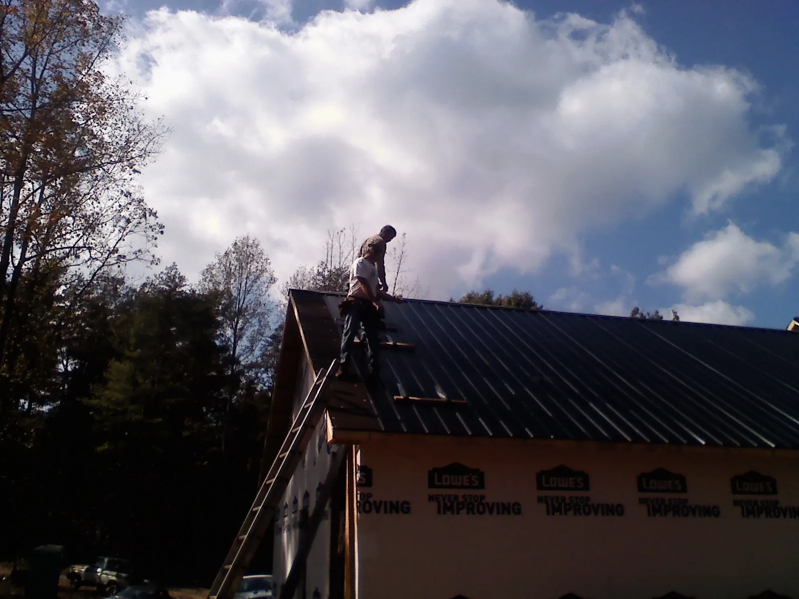Roofer fastening dark metal panels high against a cloudy sky, from a Roof Inspection job in Walnut
