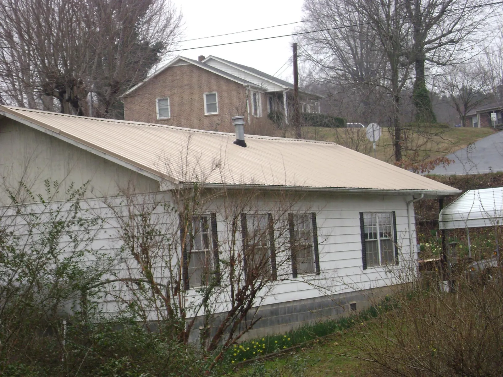 Tan metal roof on a white sided house set into a hillside — Commercial Roofing by Roofing Brothers in Walnut
